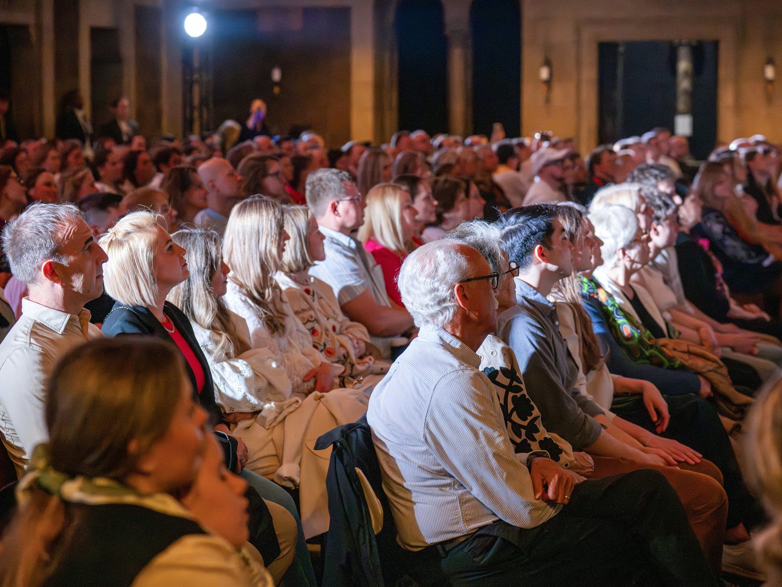 An audience seated in a dim hall, watching the stage